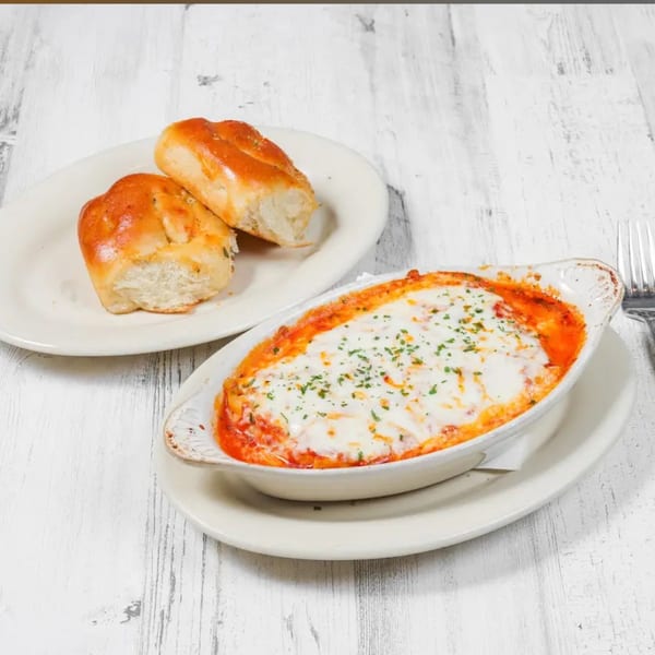 Baked ziti with melted cheese and red sauce, garnished with parsley, served with two bread rolls.