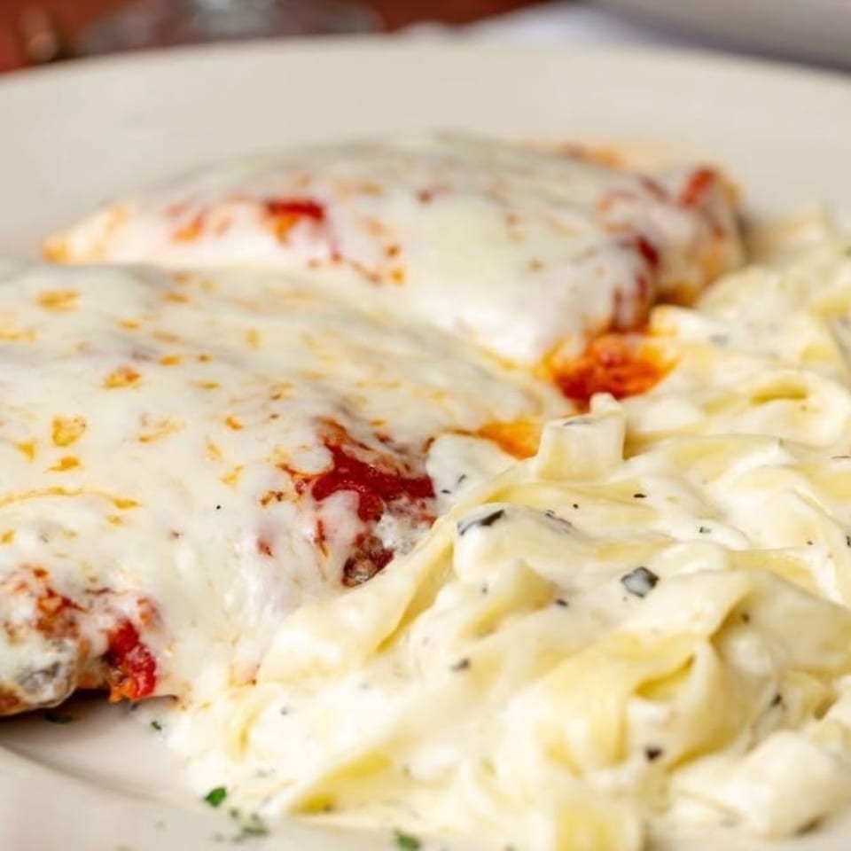 Chicken parmesan with melted cheese and red sauce, served alongside creamy fettuccine alfredo.