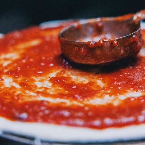 A ladle spreading rich red tomato sauce over a pizza crust at Genovas Italian Restaurant.